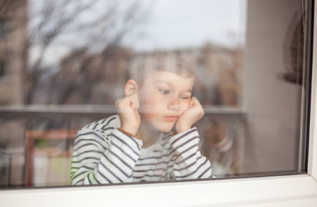 Niño aburrido mirando por la ventana sin actividades de verano que hacer